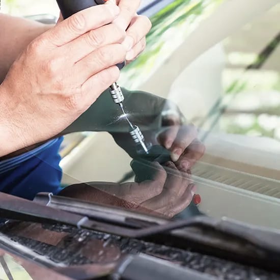 A technician’s hands injecting resin into a stone chip on a windshield.
